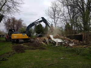 Construction equipment demolishing with wood scraps and surrounded by grass and trees