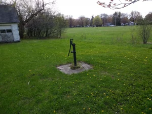 Water well surrounded by grass and trees with houses in the background