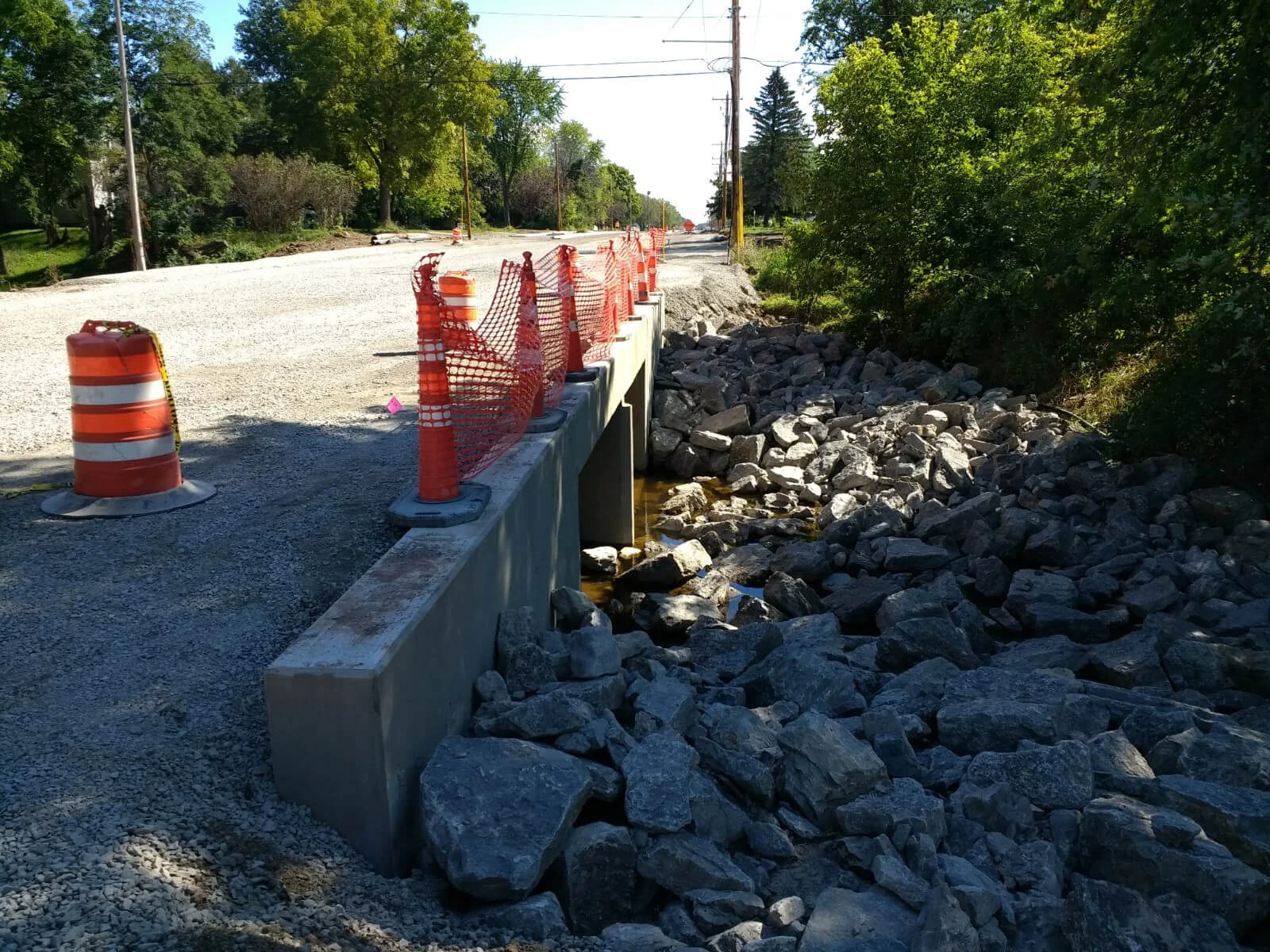 Construction cones and netting make a temporary barrier between the side of a road and a ditch full of large stones