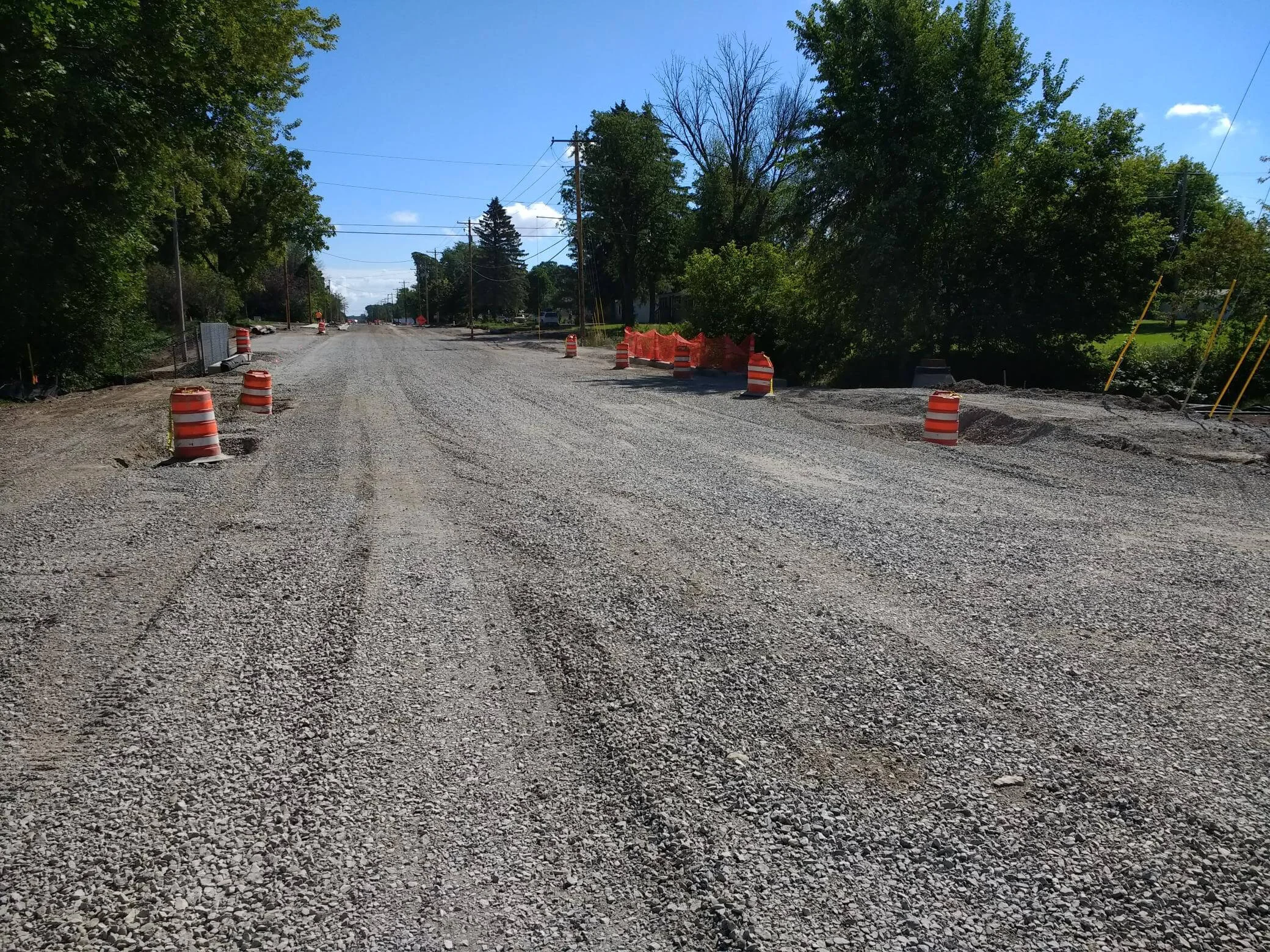 Construction barrels line the side of a wide gravel residential road
