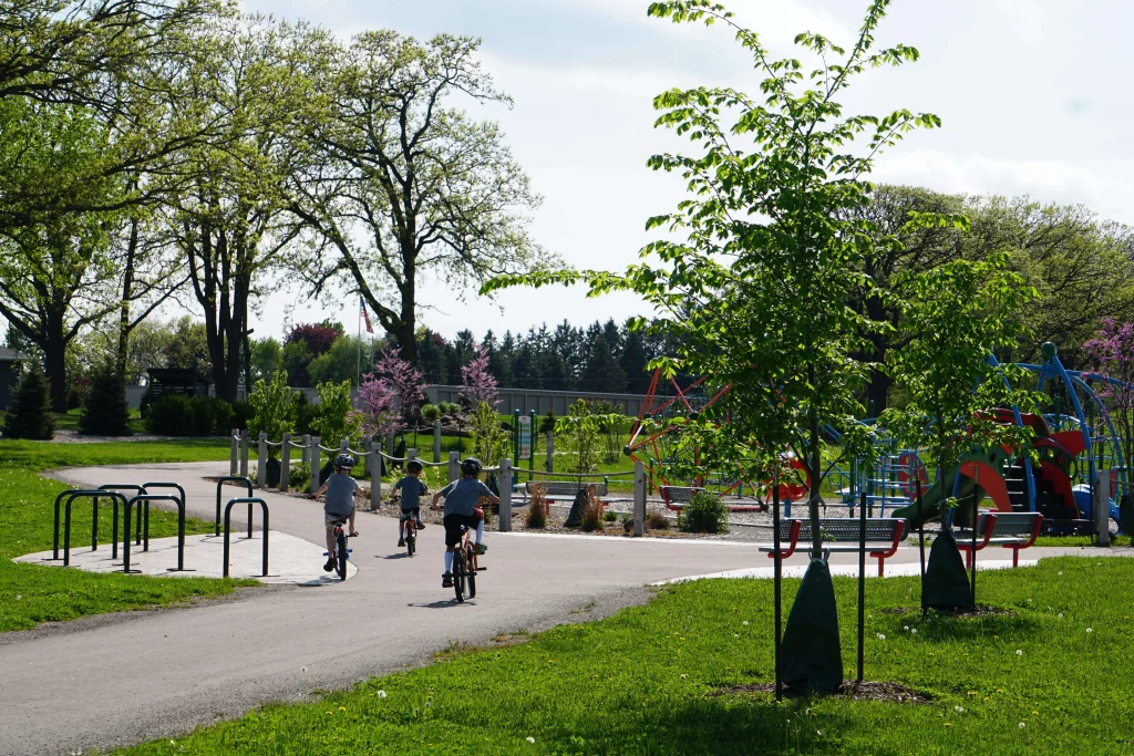 Kids riding bikes into playground surrounded by trees